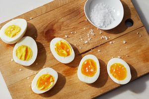 Hardboiled eggs sliced on a wooden cutting board next to a small bowl of salt