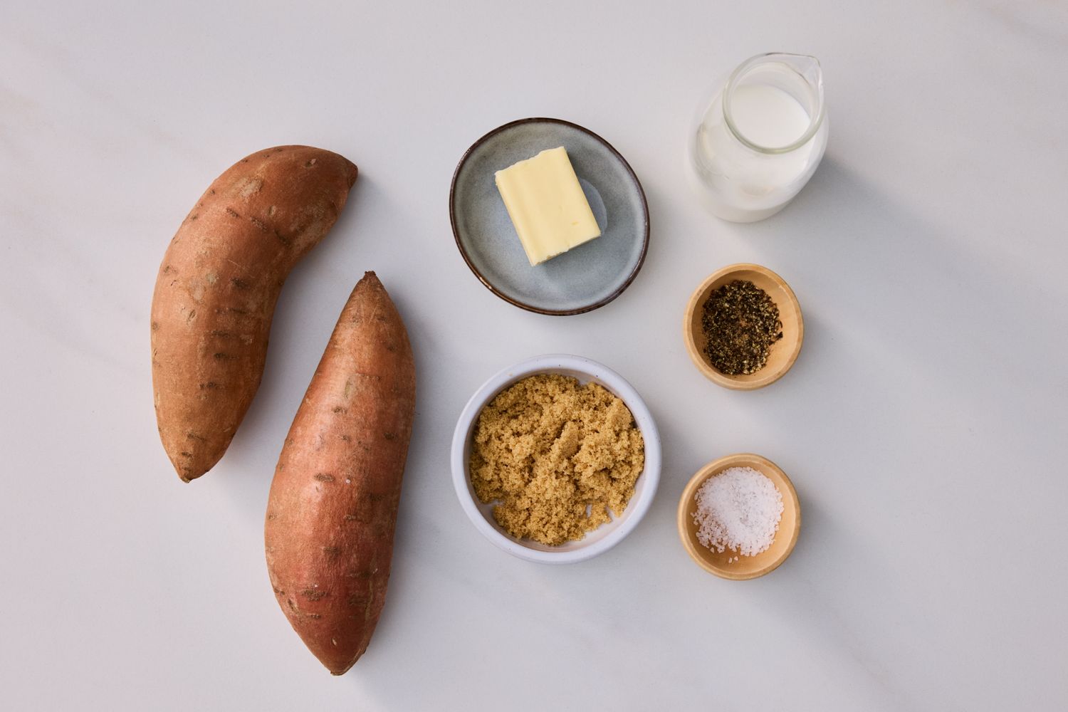 Ingredients for making mashed sweet potatoes displayed on a surface including sweet potatoes butter milk brown sugar and seasonings