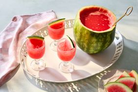 A tray with glasses of watermelon punch and a watermelon punch bowl with a ladle