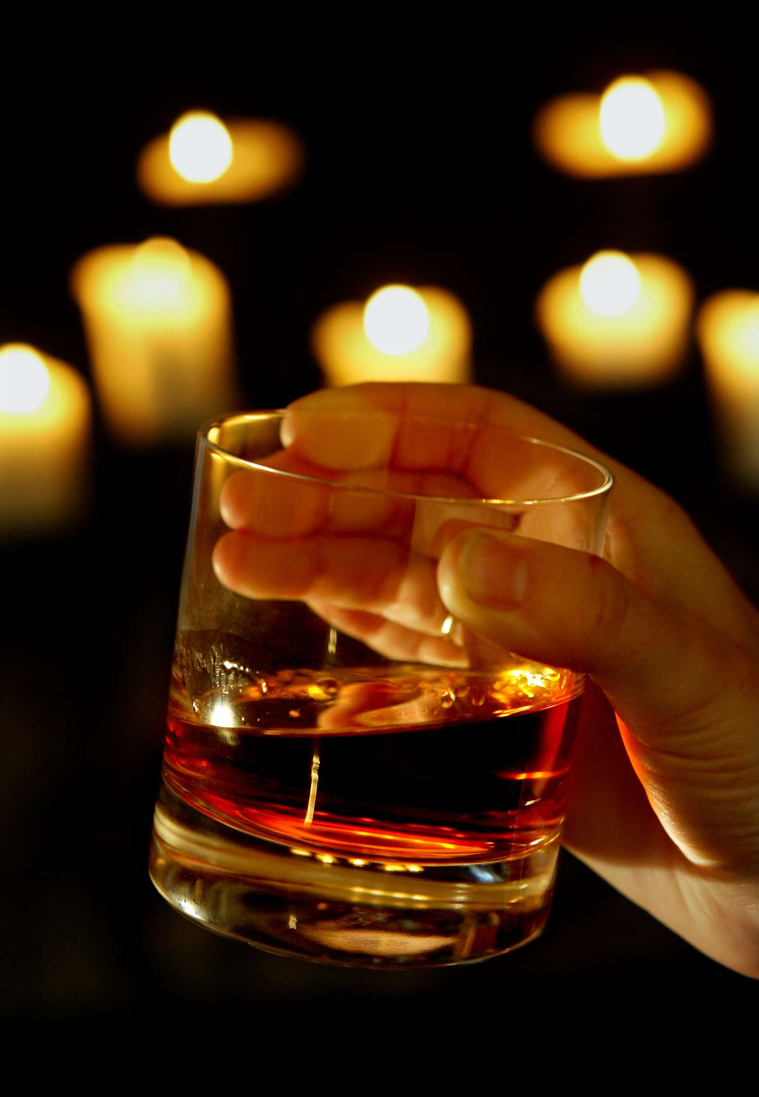 A hand holds a glass of bourbon on ice