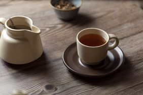 herbal tea in cup with herbs in bowl behind and teapot to left