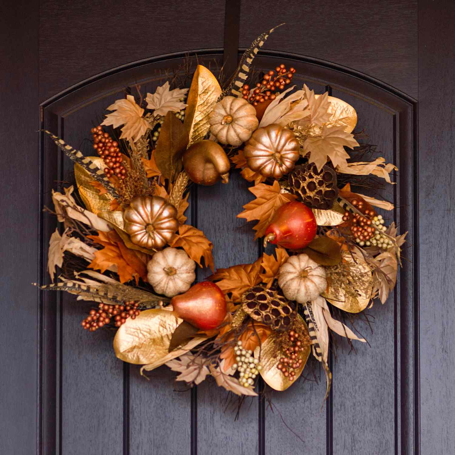 A decorative wreath featuring small gourds and autumn foliage displayed on a door