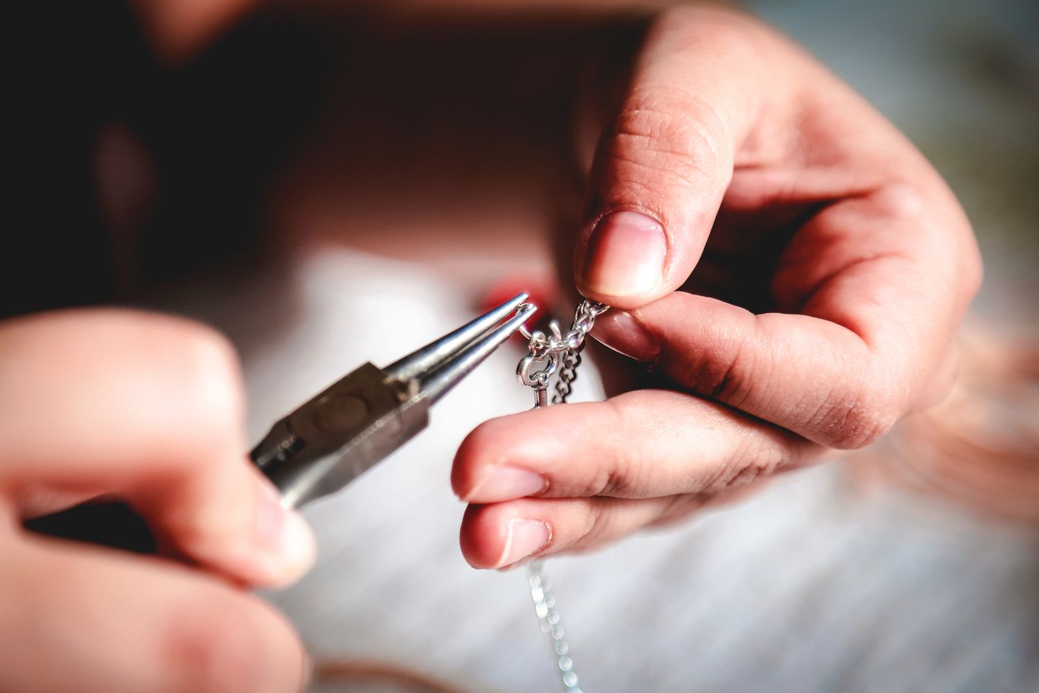 A person crafting or repairing jewelry using a pair of pliers