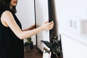 woman hanging framed art to wall