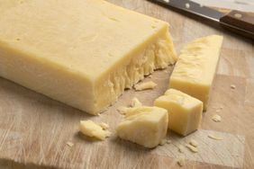 A block of cheese on a wooden cutting board partially sliced and with a knife nearby