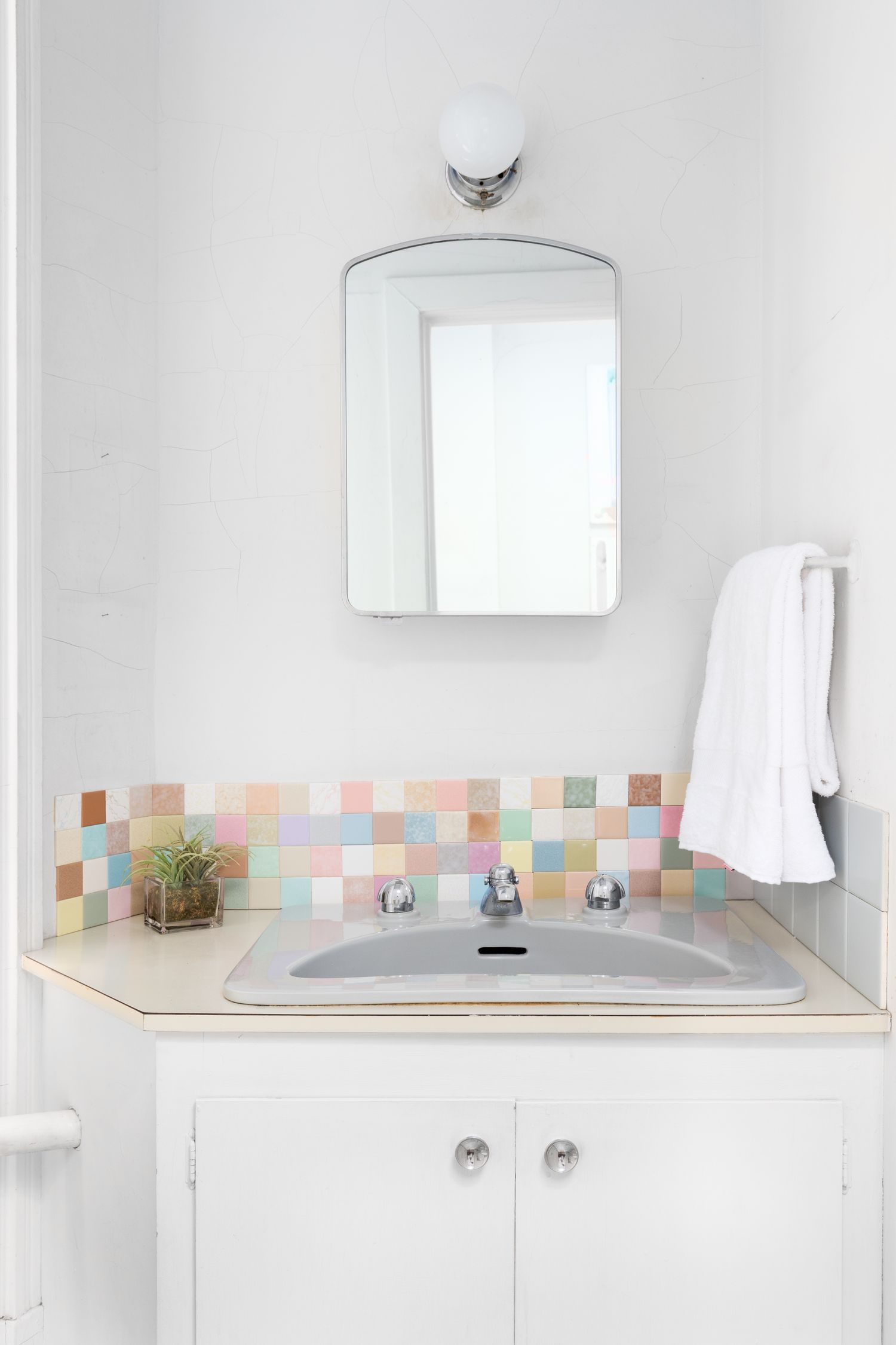 A bathroom sink with a mirror above and a colorful tiled backsplash a towel hanging on the side