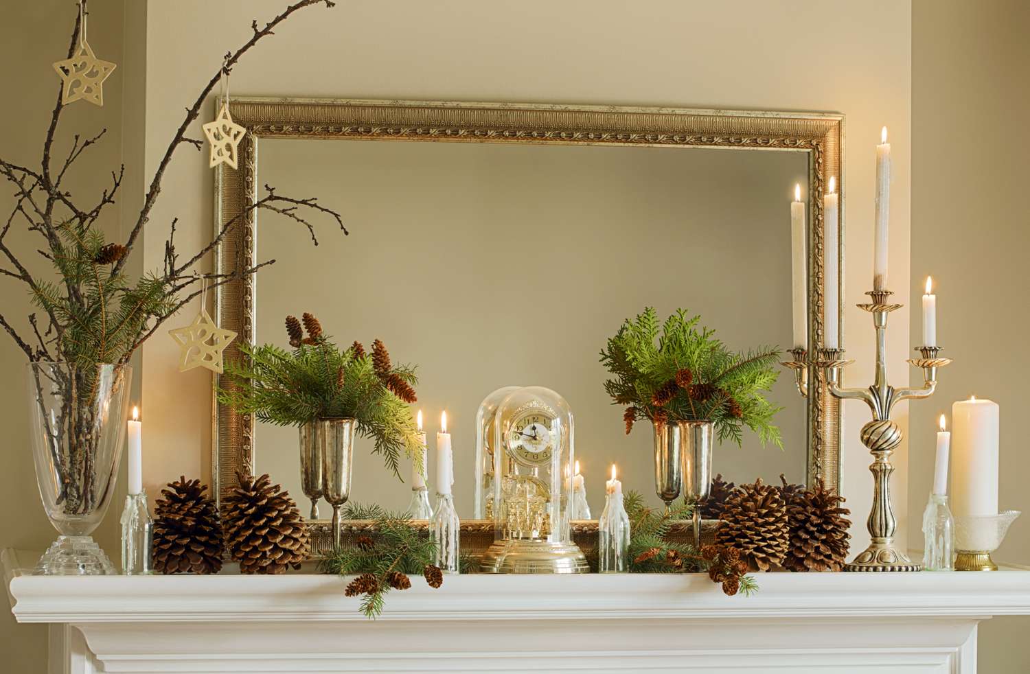 Mantel decorated with greenery pinecones candles and a mirror in the background holidaythemed arrangement