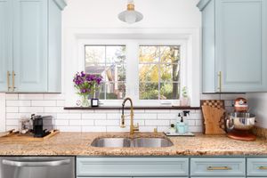 A modern kitchen sink setup with a double bowl and a view out of a window featuring cabinetry and kitchen appliances