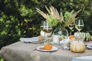 A rustic autumn table centerpiece with pumpkins wine glasses and foliage accents