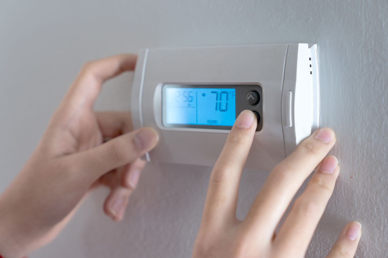 Hands adjusting a digital thermostat on a wall
