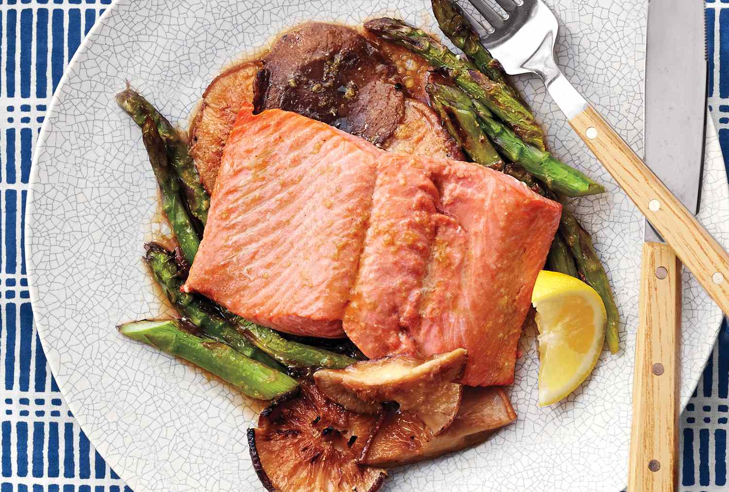 Cooked salmon served on a plate with asparagus mushrooms and a lemon wedge