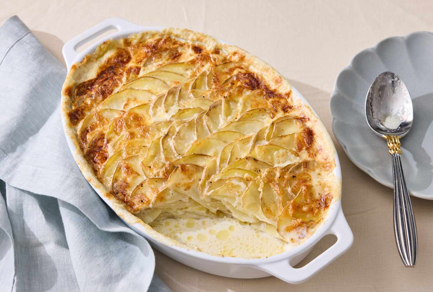 scalloped potatoes in white baking dish with a portion scooped out.