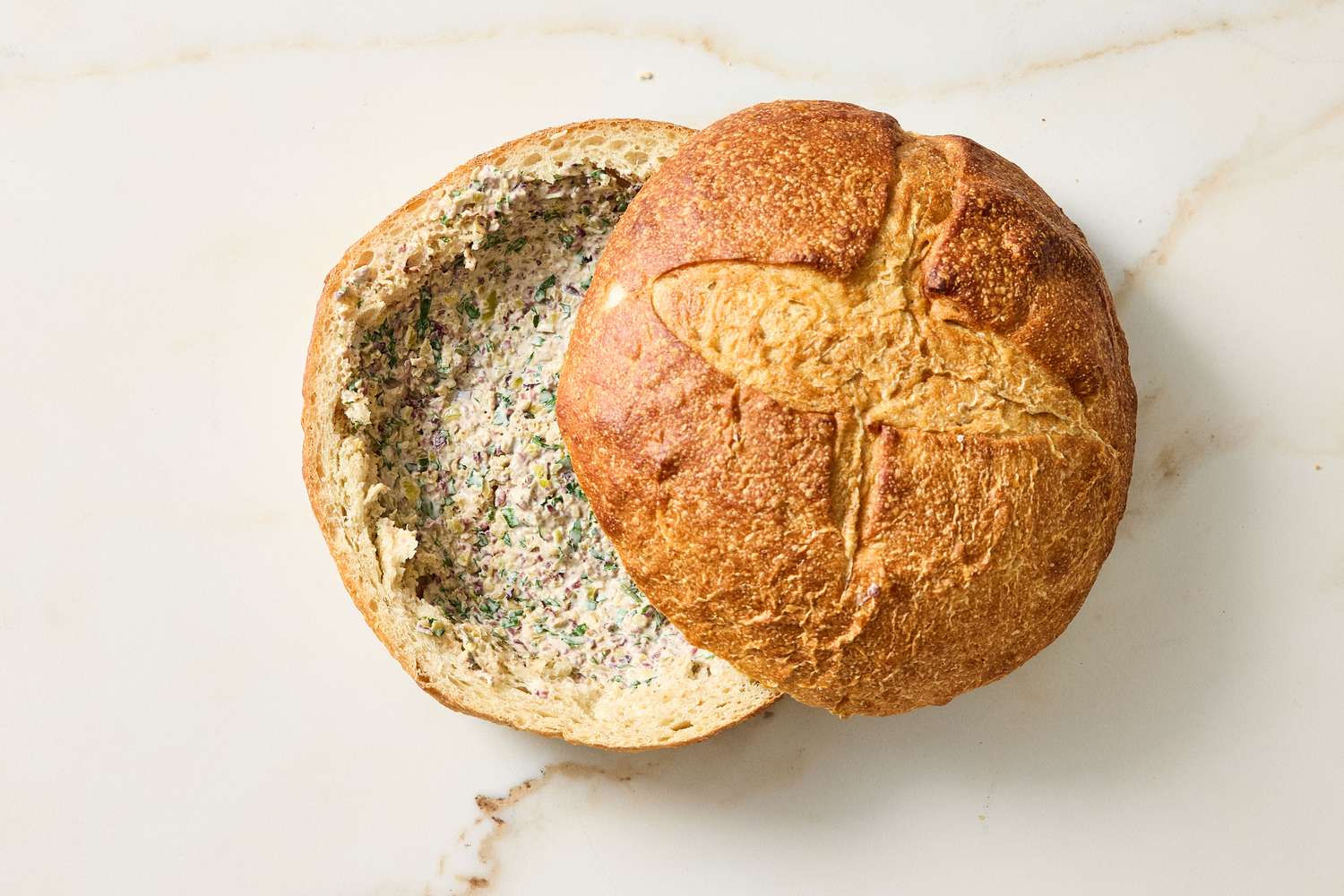 A hollowed round loaf of bread with a spread inside prepared for making a dish
