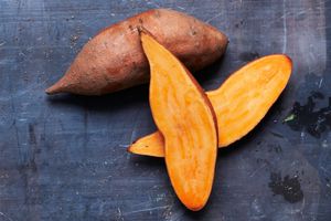 sweet potatoes, one sliced in half and one whole on dark surface