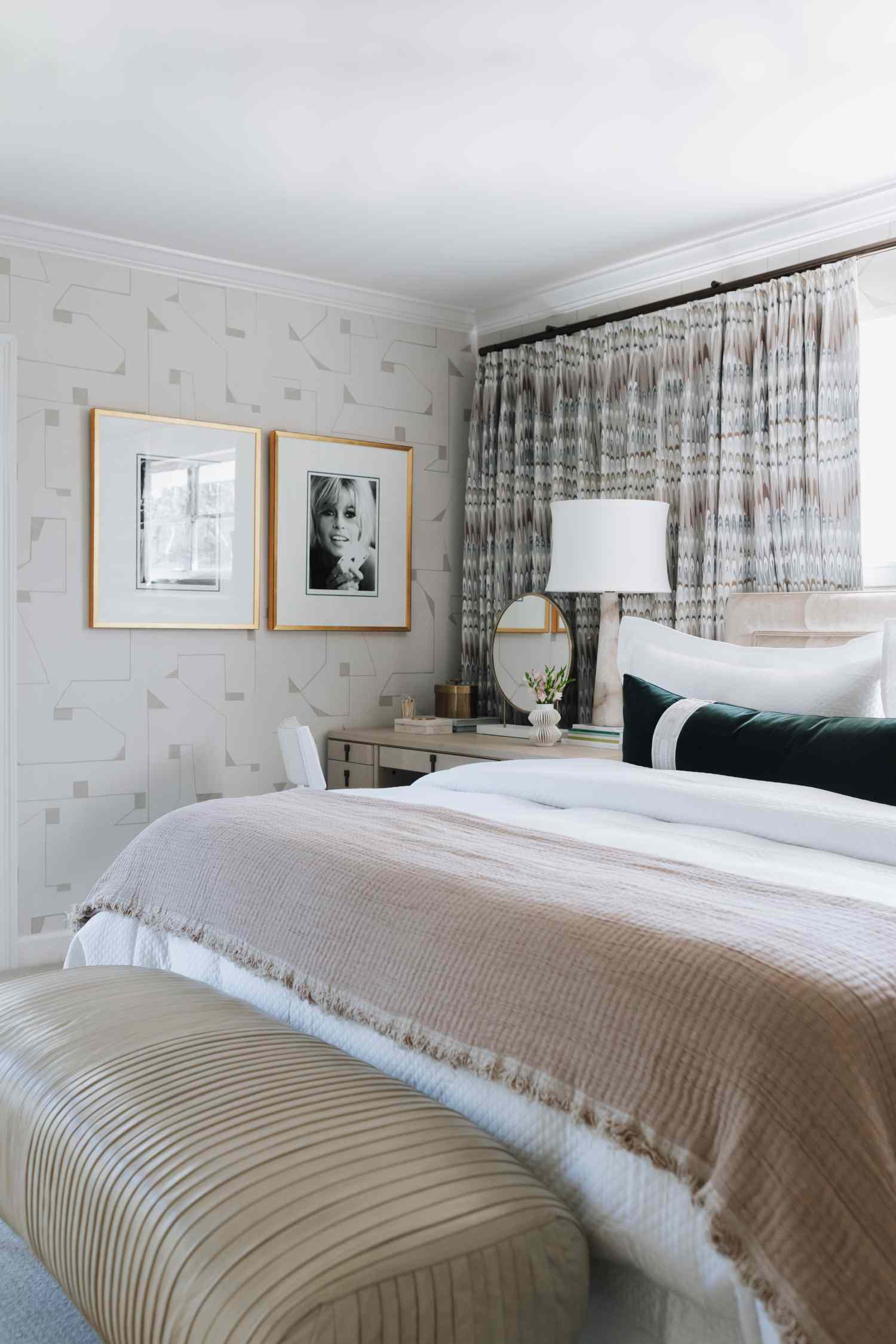 A neatly arranged bedroom with a bed decorative pillows a bench and wall art