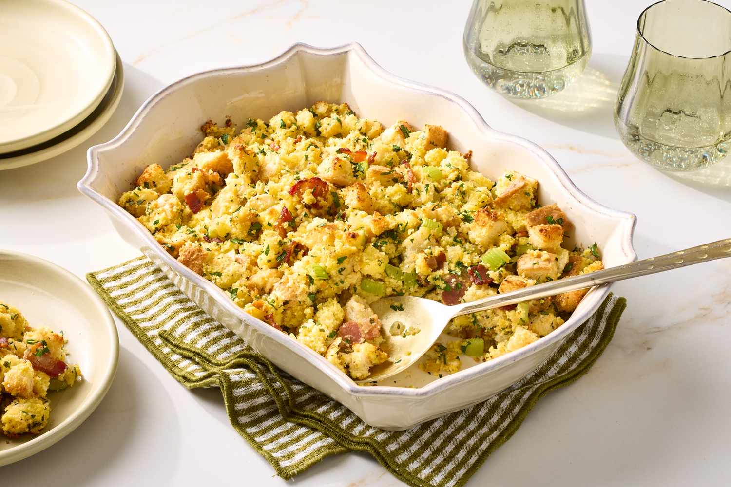 A dish containing bacon and cornbread stuffing displayed with a serving spoon