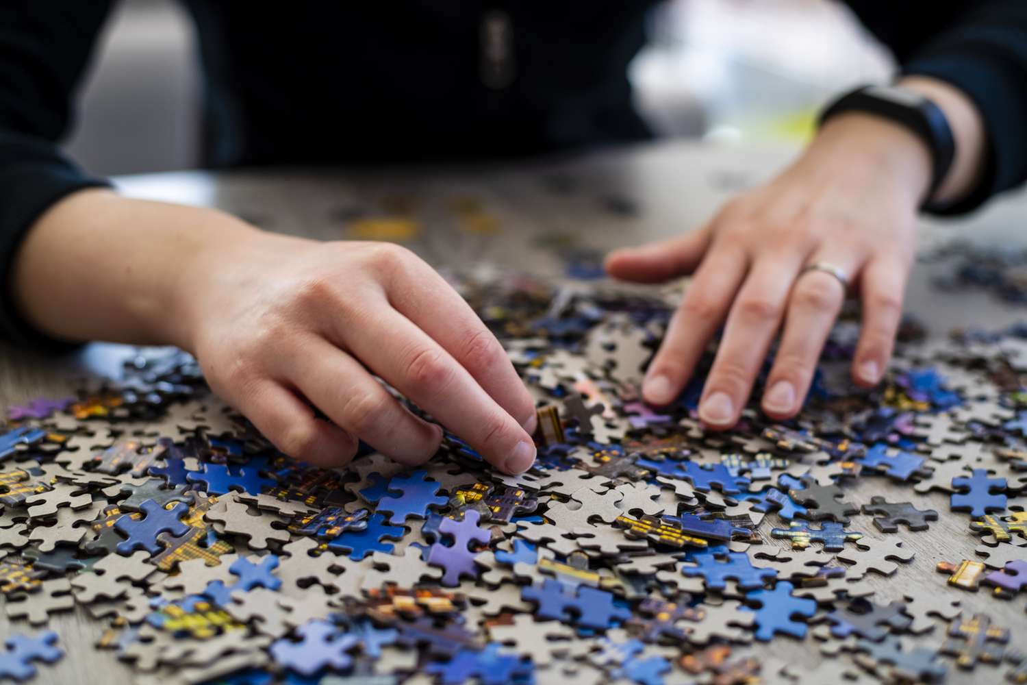 Hands sorting through jigsaw puzzle pieces on a surface