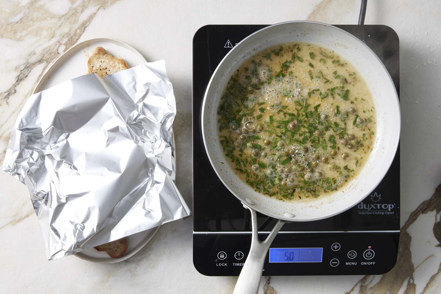 Herbs and capers soaking in white wine in frying pan