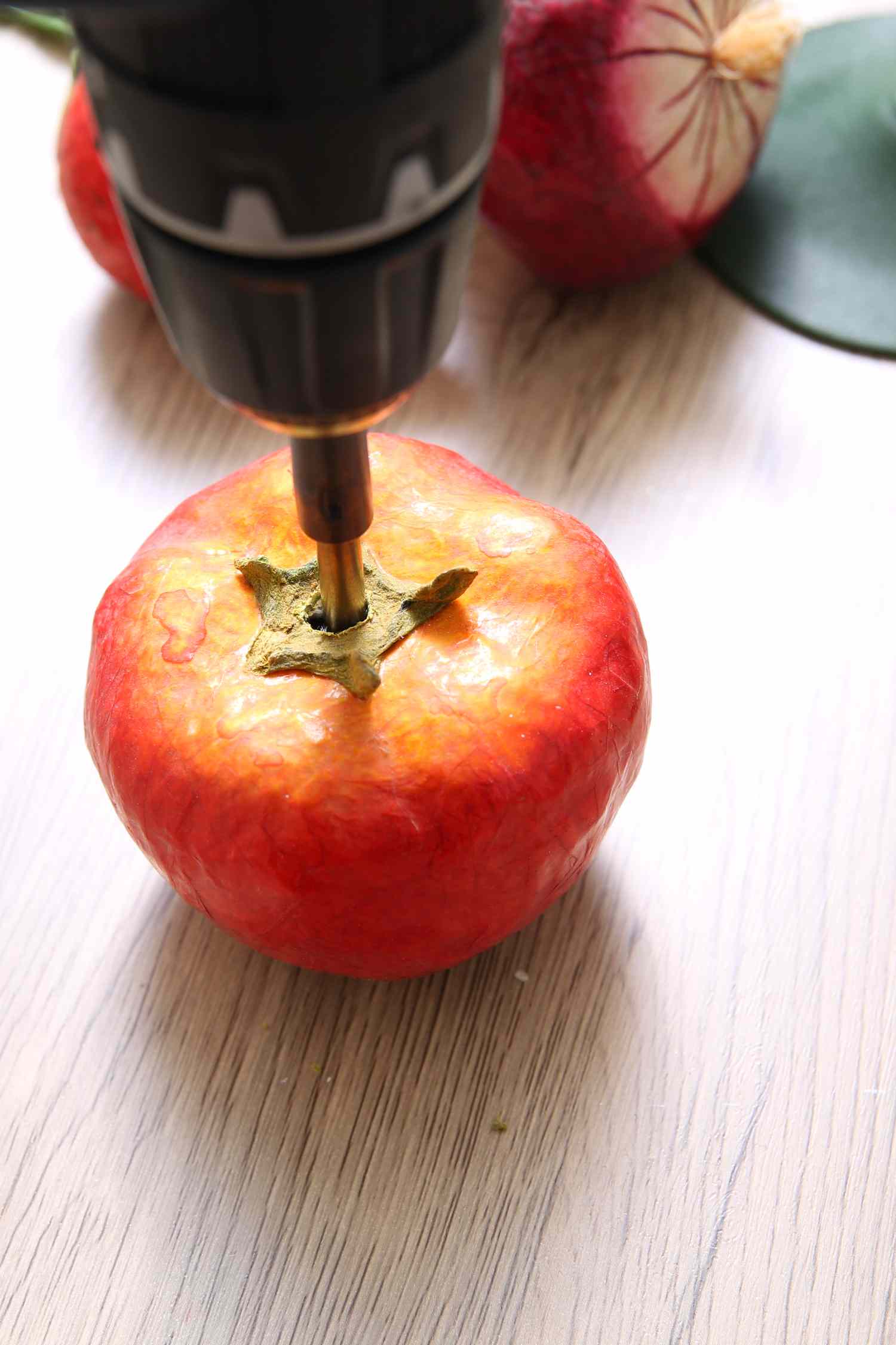 A drill inserting into an apple on a wooden surface