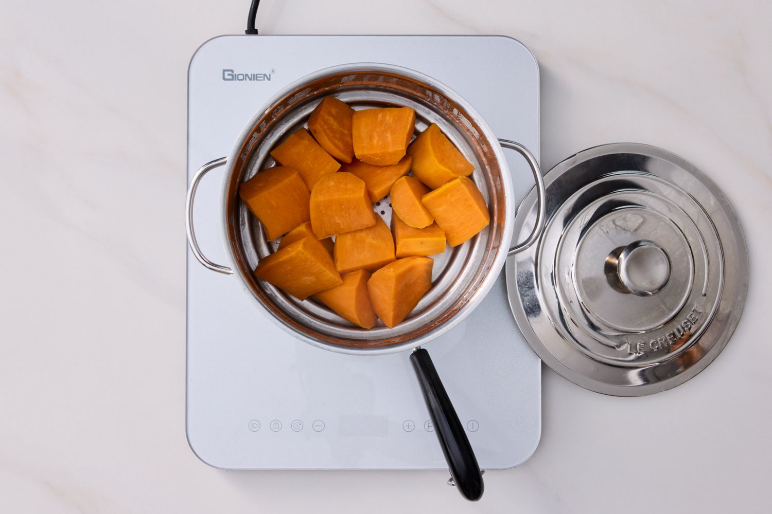 Chopped sweet potatoes steaming in a pot on an induction cooktop lid placed aside
