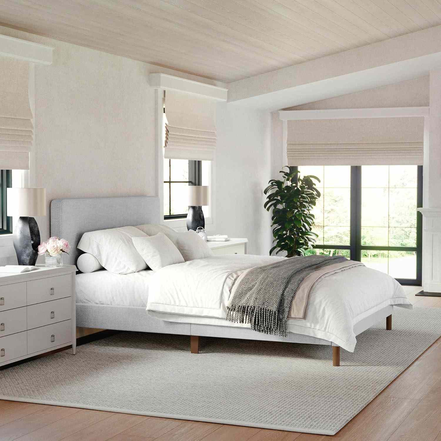 A tidy bedroom with a modern aesthetic featuring a bed nightstands and windows with blinds a decorative plant is included
