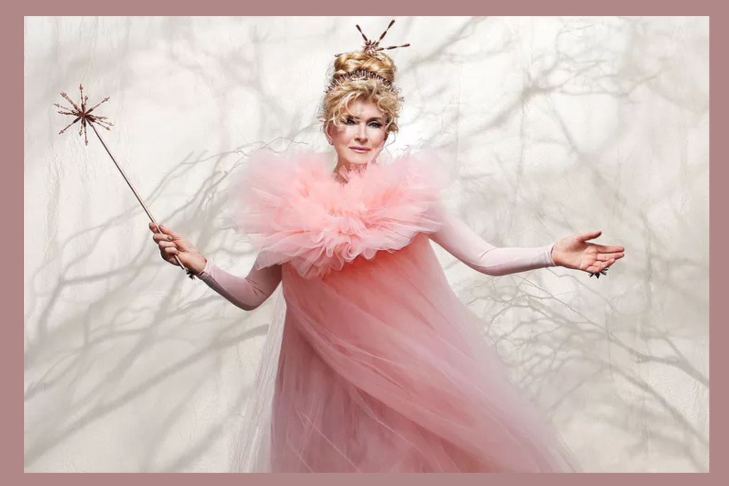 A person dressed as a fairy with a wand and ethereal attire posing with arms outstretched