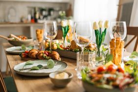 A dining table set with plates glasses croissants salads and decorative flowers