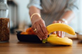 A person picking up bananas from a wooden table with other fruits visible in the background