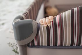 A babys hand gripping the edge of a portable crib with striped fabric