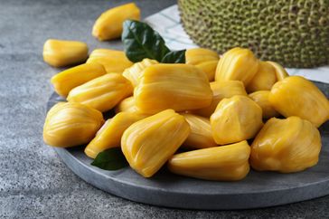 Jackfruit pieces displayed on a plate whole jackfruit in the background