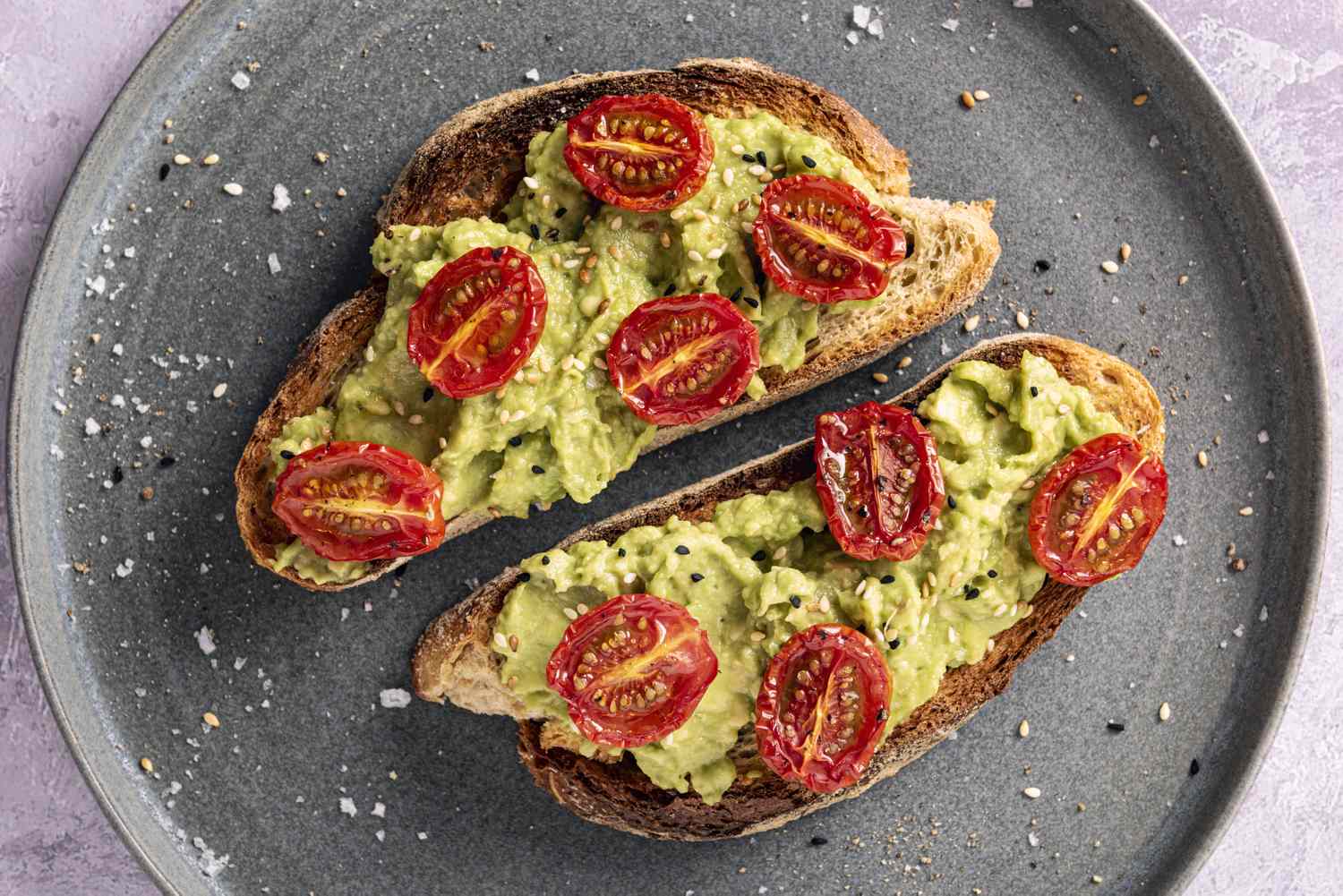 Two slices of toast topped with avocado and cherry tomato halves on a plate