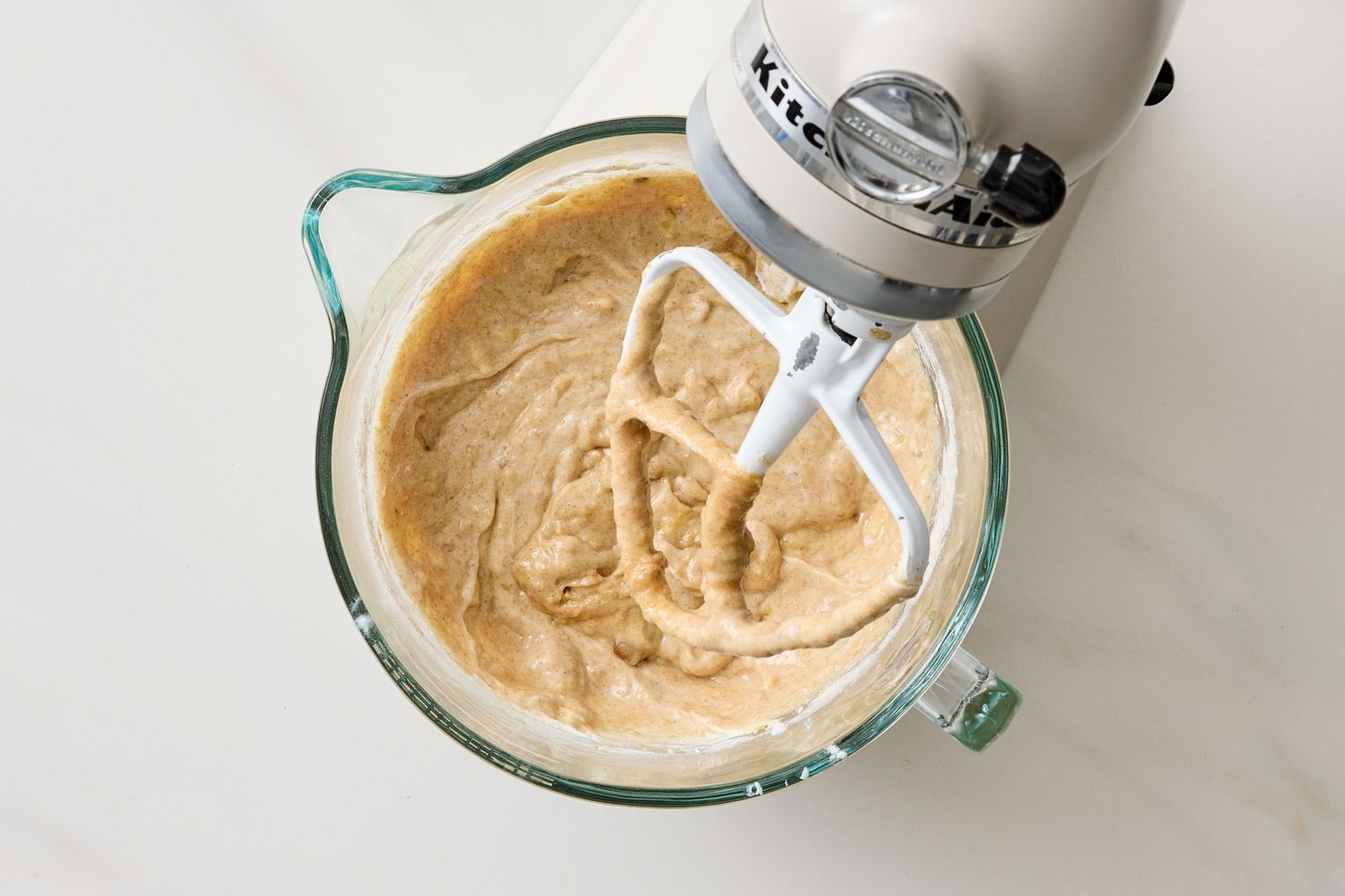 Banana muffin batter in a stand mixer bowl with the paddle attachment
