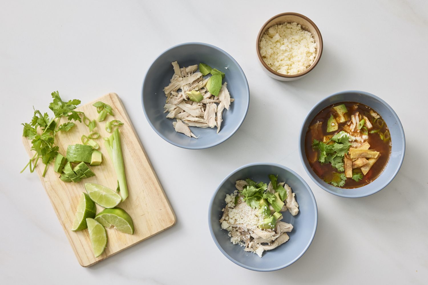 Ingredients and preparation for a Mexican chicken tortilla soup with bowls of soup components and a cutting board with toppings