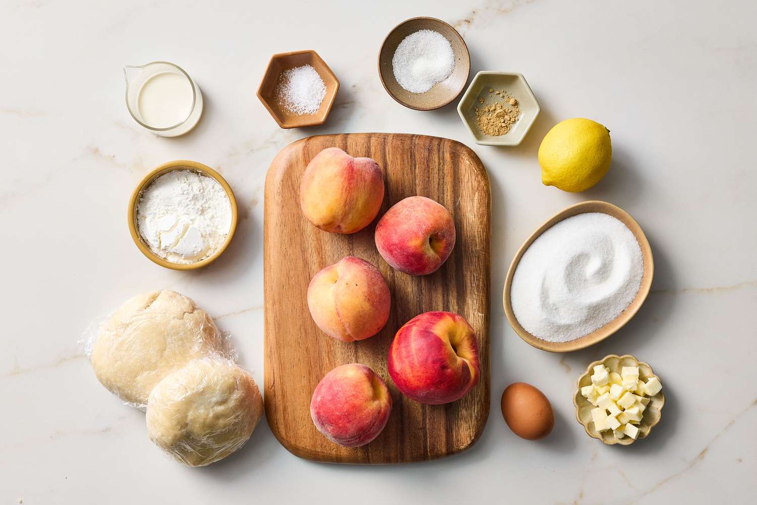 Ingredients for making peach pie arranged on a surface including peaches sugar flour butter lemon and pastry dough