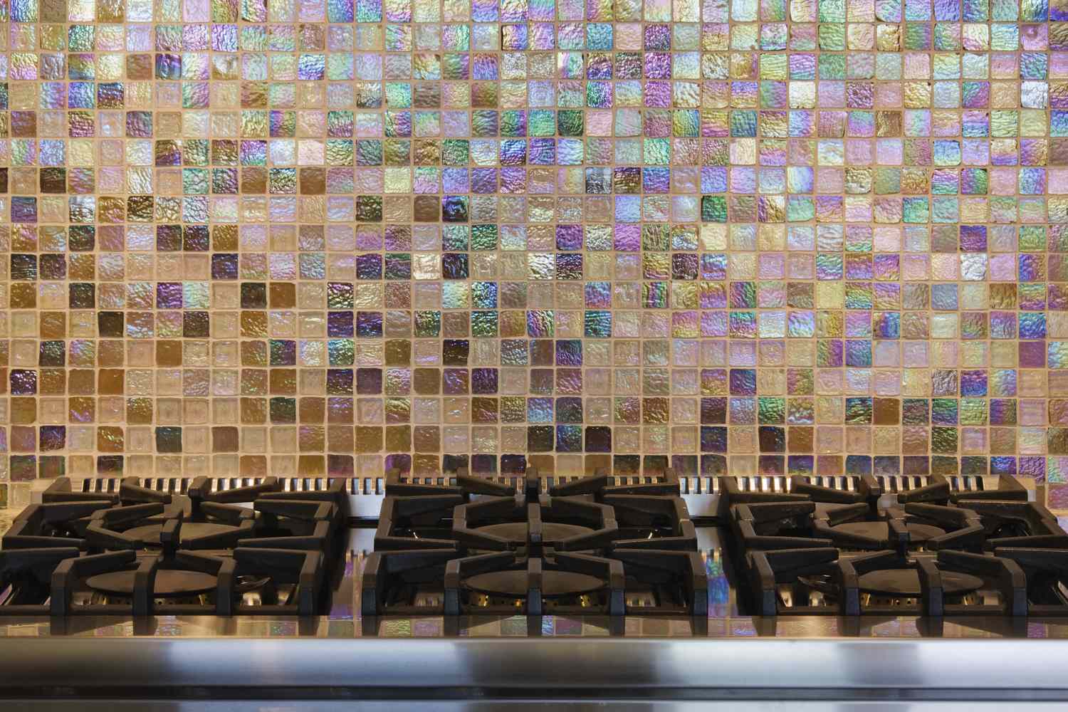 A kitchen stovetop with a tiled backsplash featuring iridescent square tiles