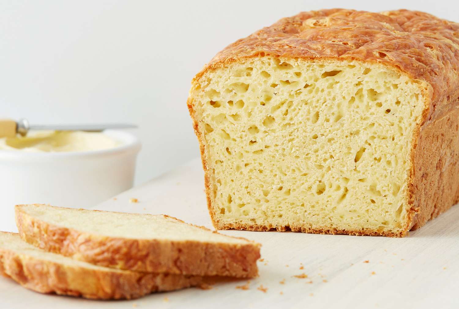 A loaf of bread with slices cut on a wooden surface butter in a container in the background
