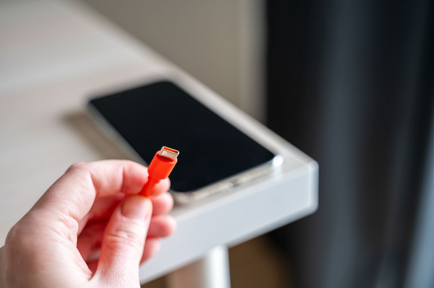 Hand holding orange Type C charging cable for smartphone