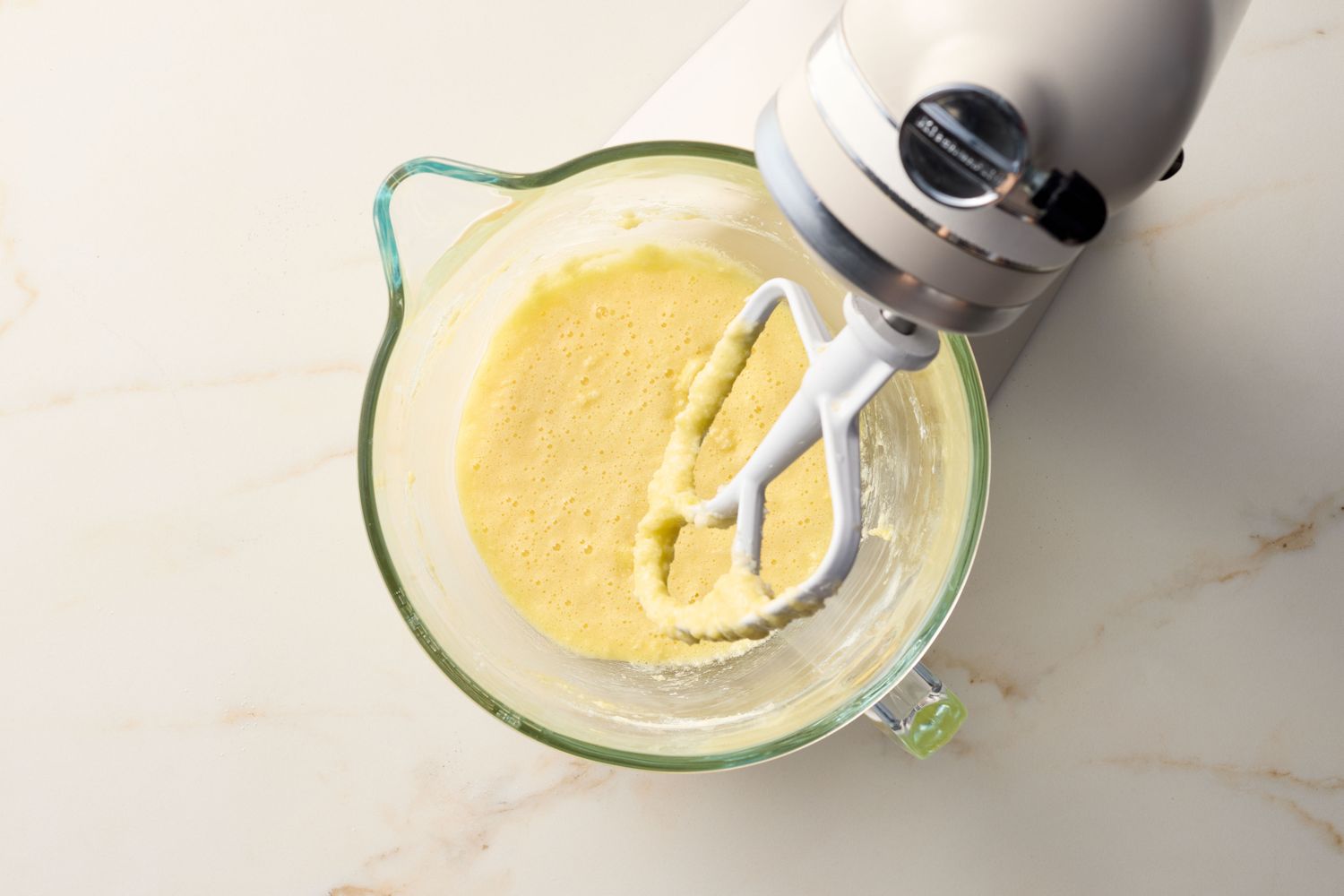 A glass mixing bowl with batter and a stand mixer paddle attachment on a countertop