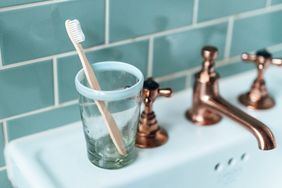 A toothbrush in a glass cup on a bathroom sink beside a faucet