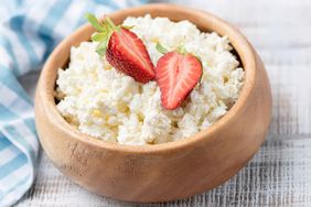 A wooden bowl of cottage cheese topped with two strawberry halves
