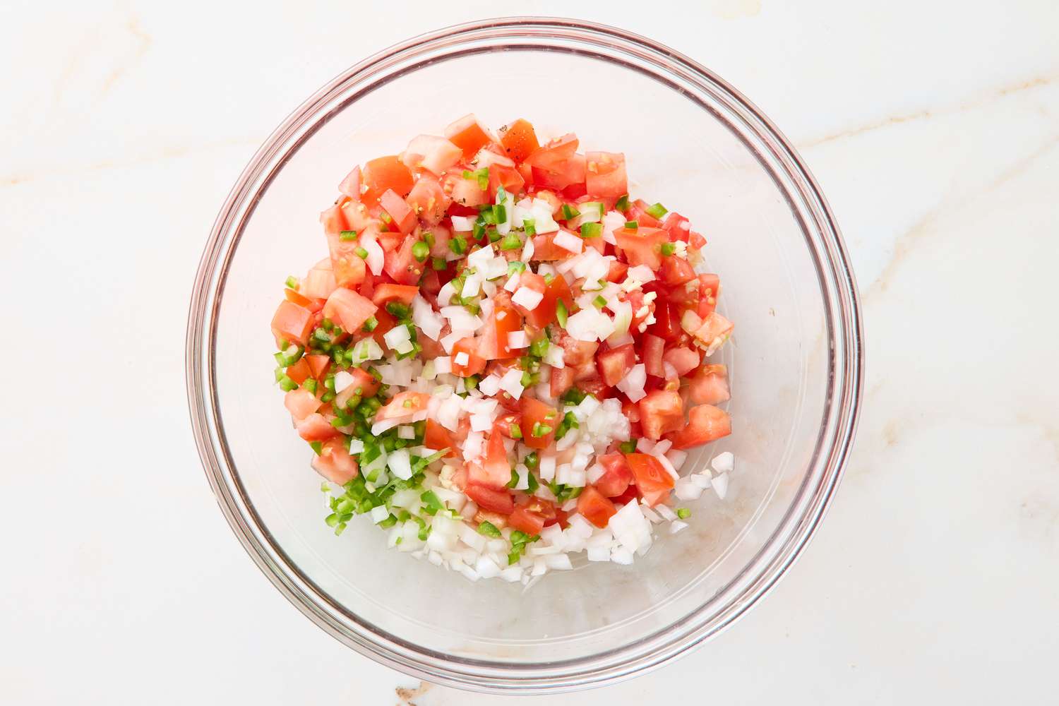 A glass bowl filled with diced tomatoes, onions, and chopped green chilies
