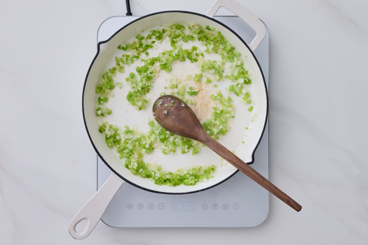 A pan with sliced green onions sauting in a white sauce on a stovetop