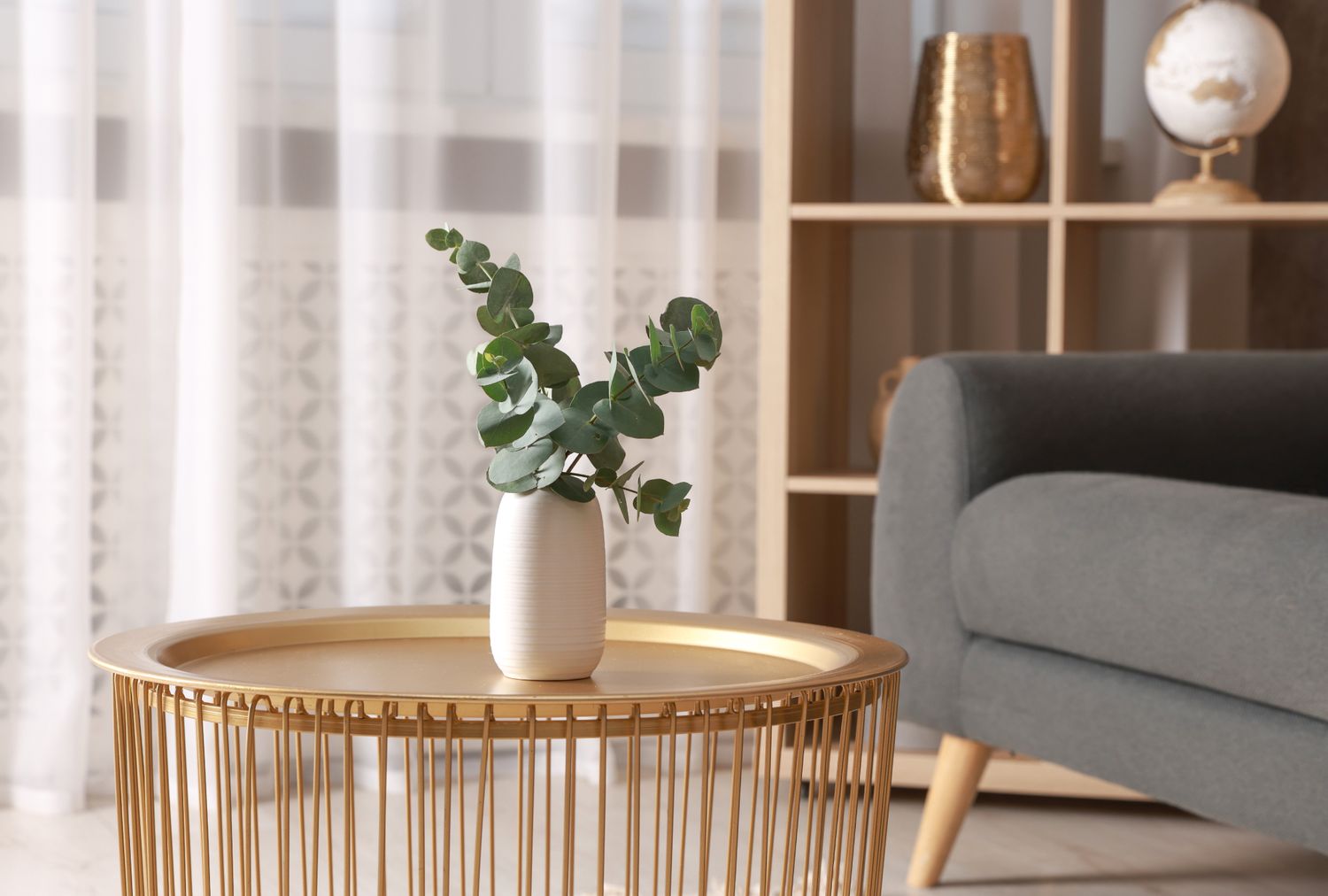 A round gold coffee table with a vase of greenery placed in a living room setting