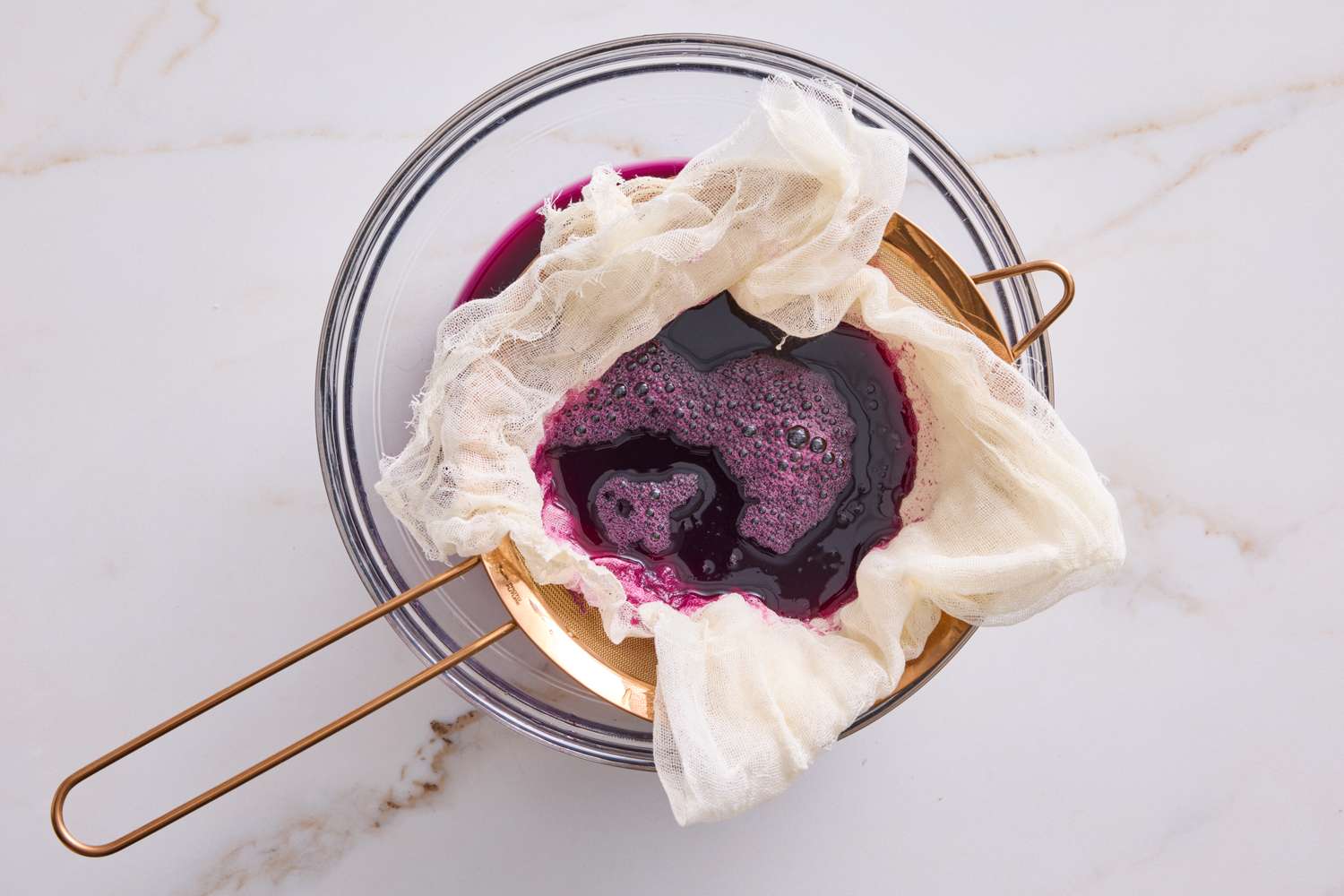 Strained fruit juice in cheesecloth over a strainer for jelly preparation
