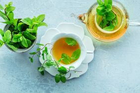 A cup and teapot of herbal tea with mint leaves alongside a pot of fresh mint
