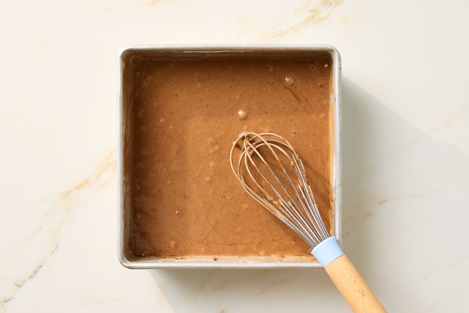 A baking pan filled with chocolate cake batter and a whisk resting on it