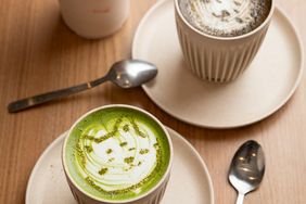 Two ceramic cups of drinks one a matcha beverage and the other a latte placed on saucers on a wooden table with spoons