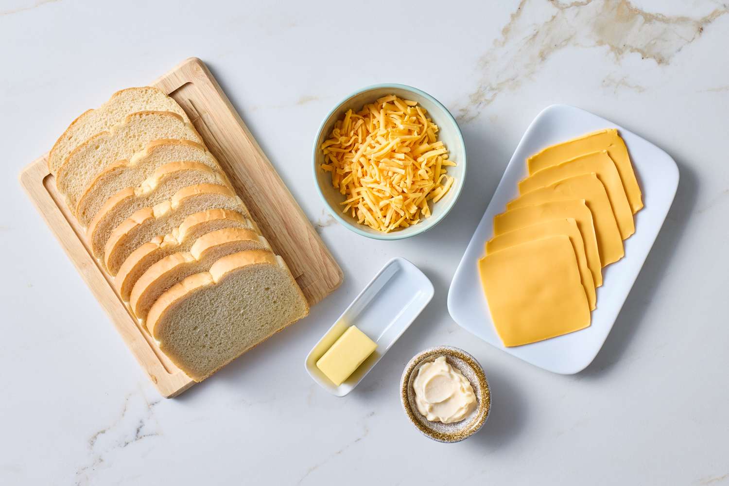 Ingredients for grilled cheese including sliced bread shredded cheese sliced cheese butter and mayonnaise