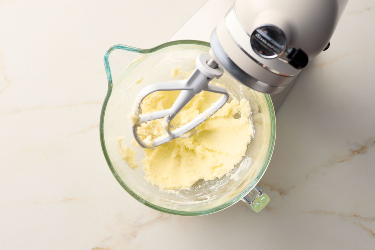 An electric mixer blending ingredients in a glass bowl on a countertop