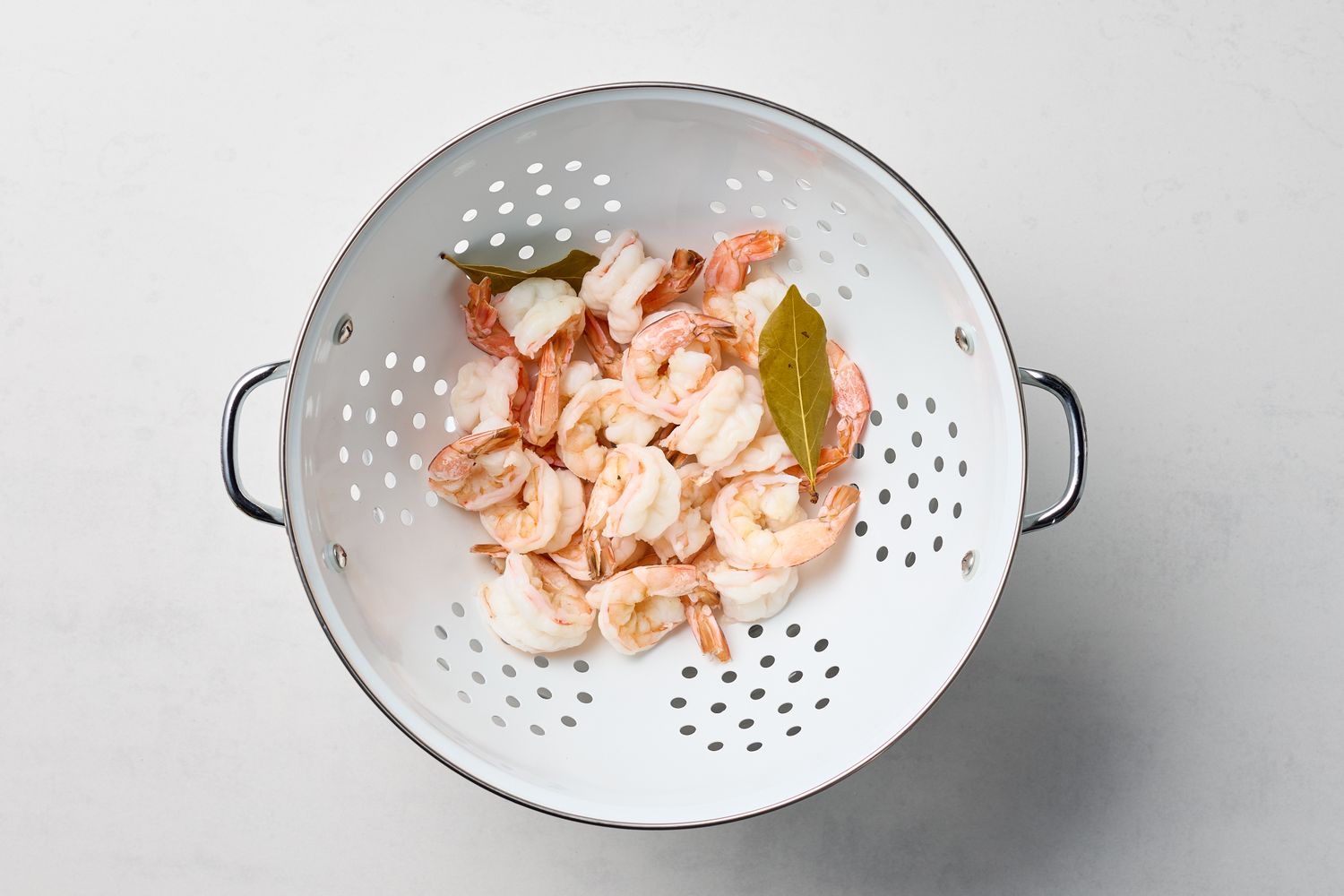 Cooked shrimp in a colander with bay leaves